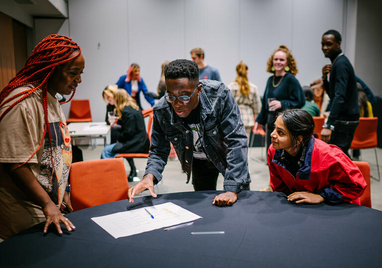 Group of people hovering around a table with a black cloth looking at a piece of paper