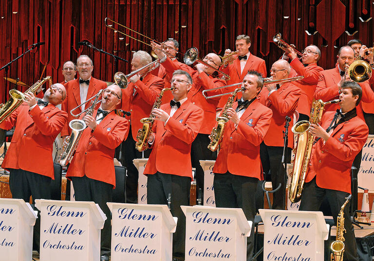 The brass section of the Glenn Miller Orchestra performing on stage, with the double bassist in the background