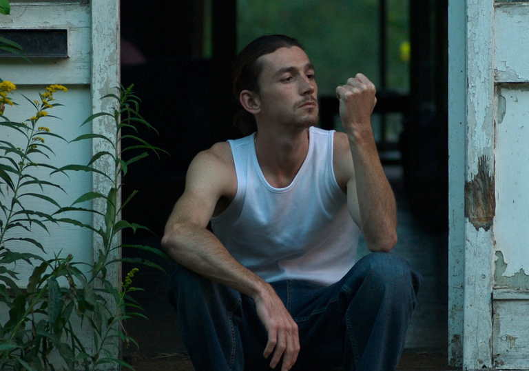 A man sits in a peeling doorway at dusk