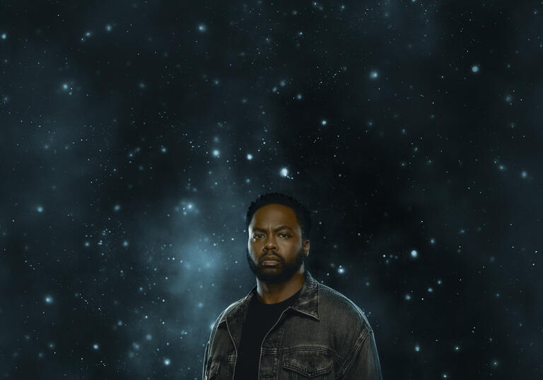 A man looks forward intensely against a dark sky filled with stars