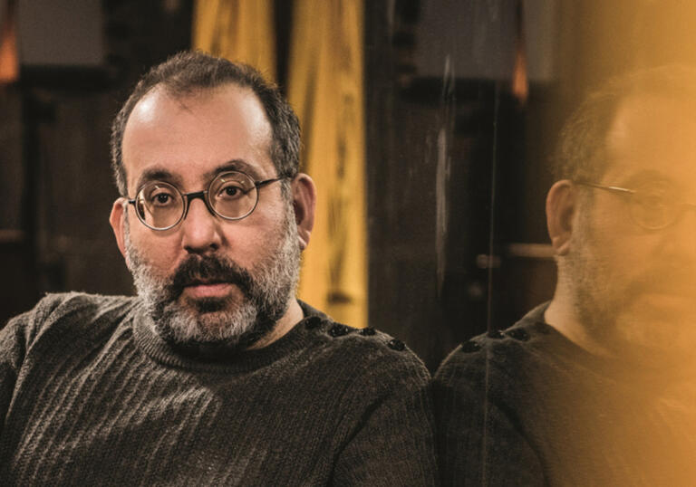 A man with a beard and glasses sits in a room looking forward