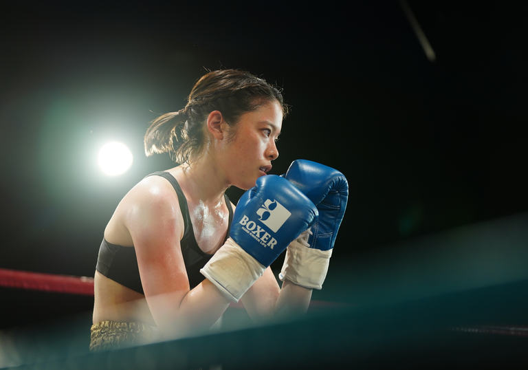 A woman stands ready to punch in a dark boxing ring