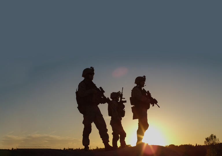 Three soldiers standing in silhouette against sunrise