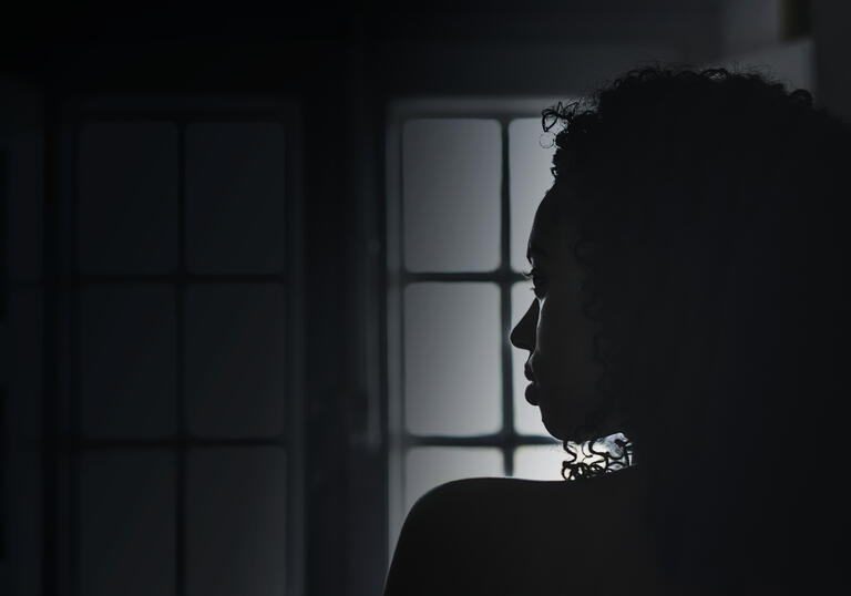 Silhouette of woman in profile looking over her shoulder in dark room with window in background