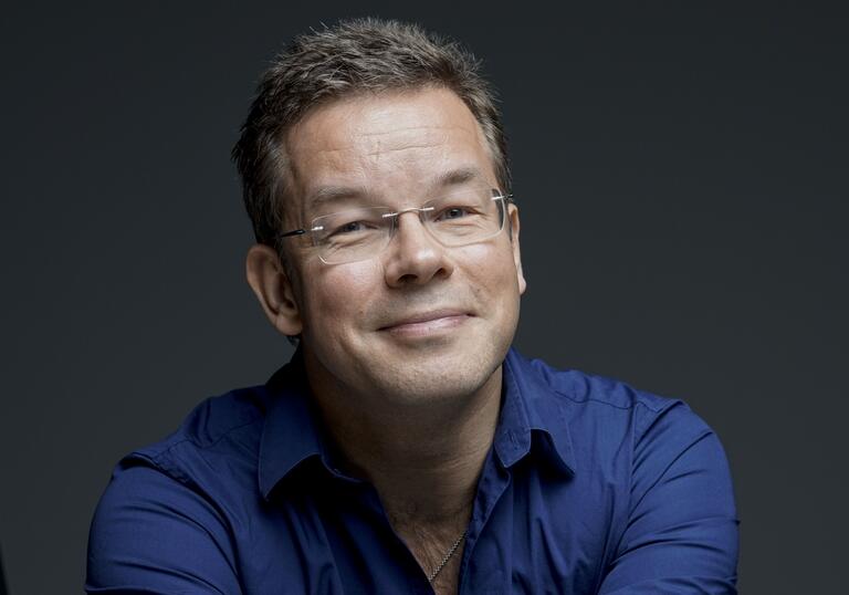 Antony Hermus smiling at camera wearing blue shirt and glasses