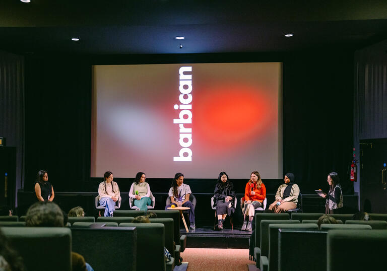 image of a panel seated in front of a cinema screen which has the Barbican logo displayed