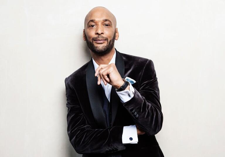 Tommy Blaize wearing black velvet jacket looking at camera with one hand near 