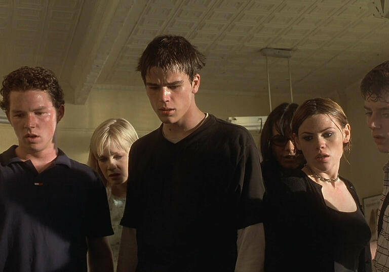  A group of teens stand in a hall looking concerned