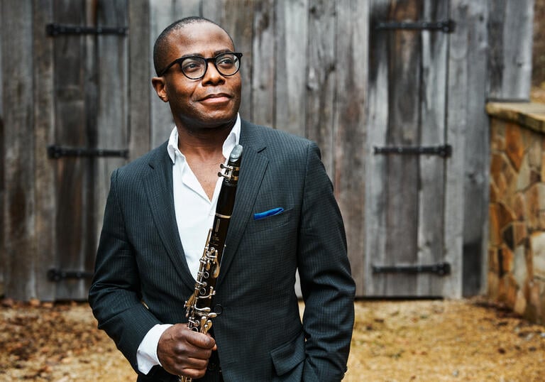 Anthony McGill standing in front of a wooden barn holding his clarinet