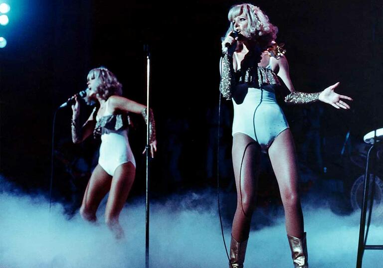 Members of the band ABBA dance in hot pants on a dark stage