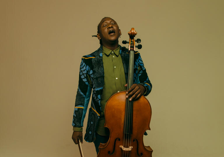 Abel Selaocoe looking upwards with his eyes closed, holding his cello
