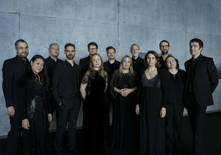 Members from Collegium Vocale Gent dressed in black, standing in front of a concrete wall