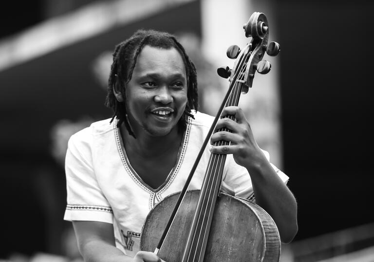 Black and white photo of Abel Selaocoe holding his cello
