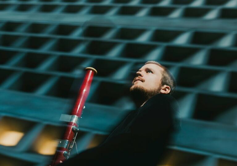 Mathis Stier holding his bassoon in front of a concrete building