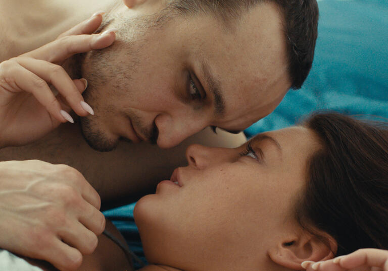 A man and a woman embrace intimately in bed.