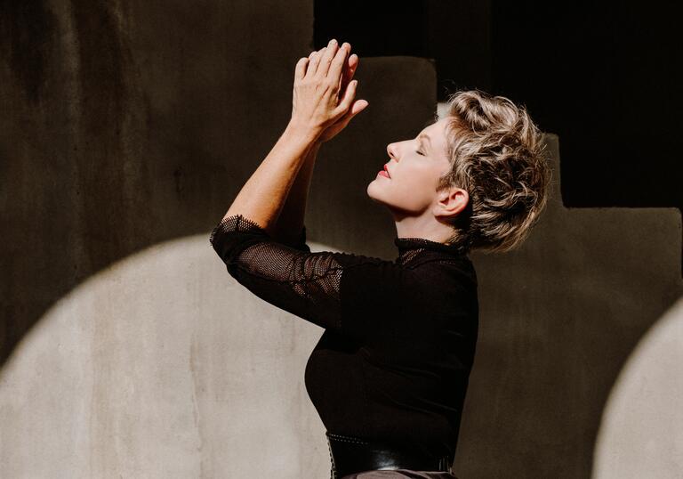 Side profile of Joyce DiDonato with her hands clasped and raised upwards