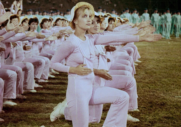 A group of cheerleaders in pink and white dresses do a choreographed dance.