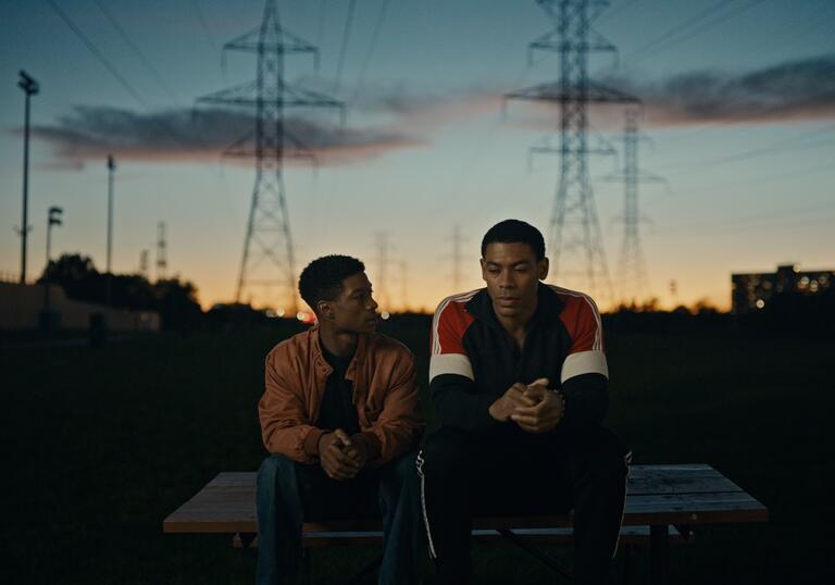 Two brothers sit on a wall against a sunset backdrop.