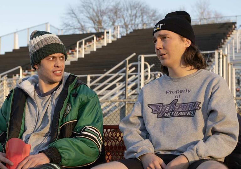 Two young men sit on bleachers looking at each other.