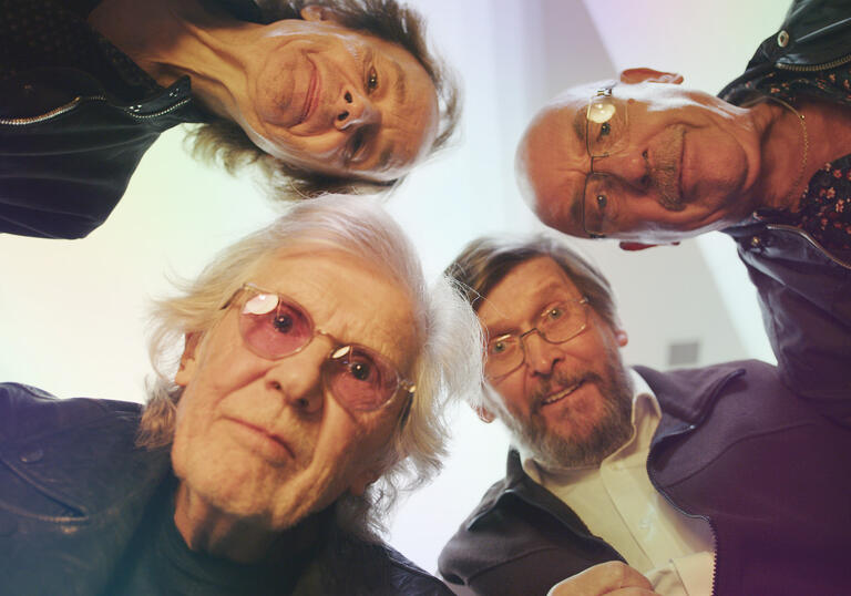 The members of the rock band The Zombies peer into the camera which is on the floor.