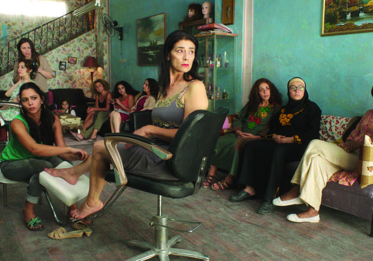A group of women sit around in a hair salon looking annoyed. 