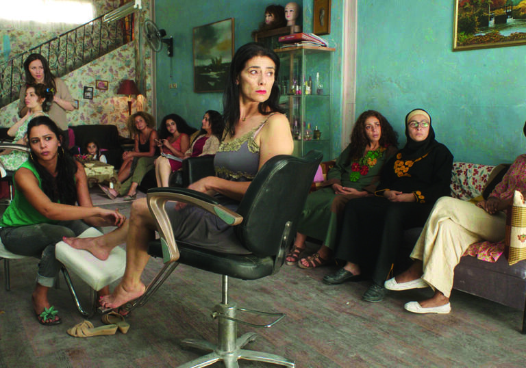 A group of women sit around in a hair salon looking annoyed.