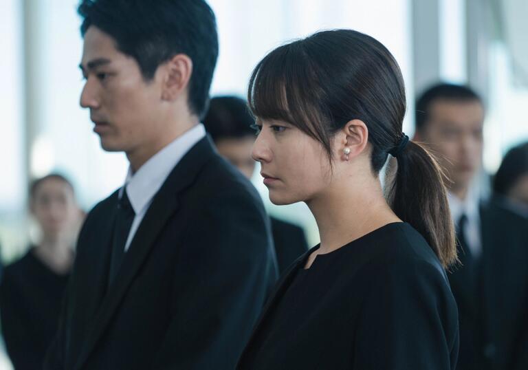 A man and a woman stand next to each other in funeral wear.