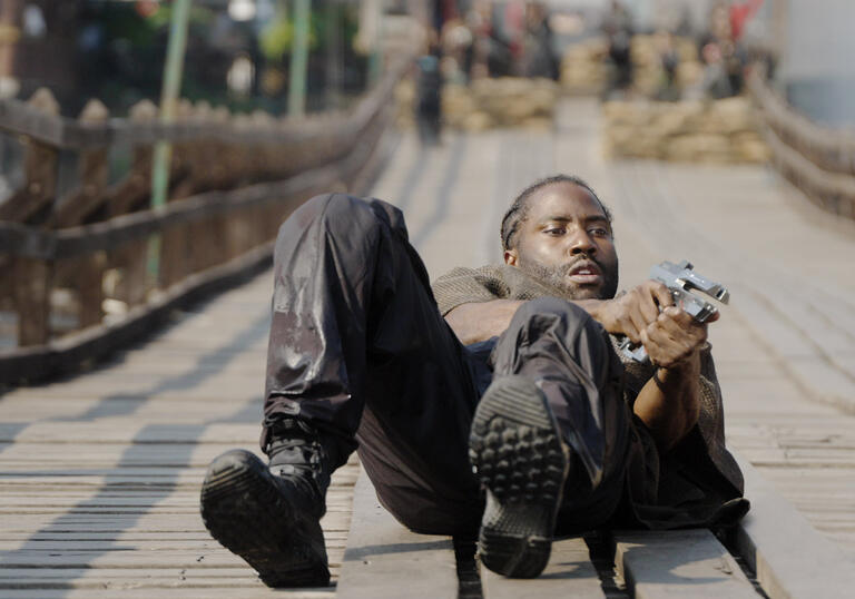 A soldier holds a gun in his hand whilst lying on the floor, ready to shoot. 