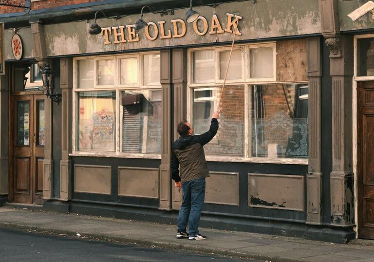 A man uses a long pole to try fix a falling letter on a sign for a derelict pub.