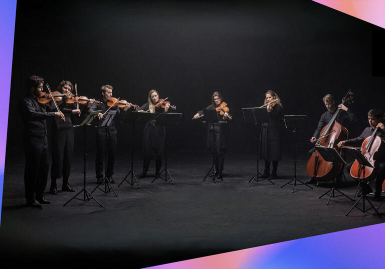 The United Strings of Europe performing on a black stage, with pink and blue triangular blocks framing the photo