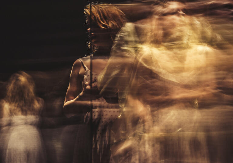 A mystical image of a woman moving across a stage, in a ghostly manner. 