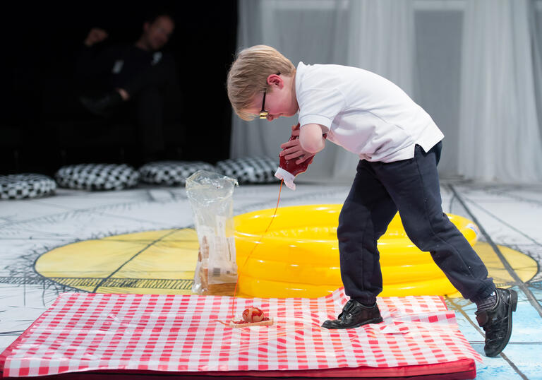 A child walks over a picnic blanket while looking at something on the floor