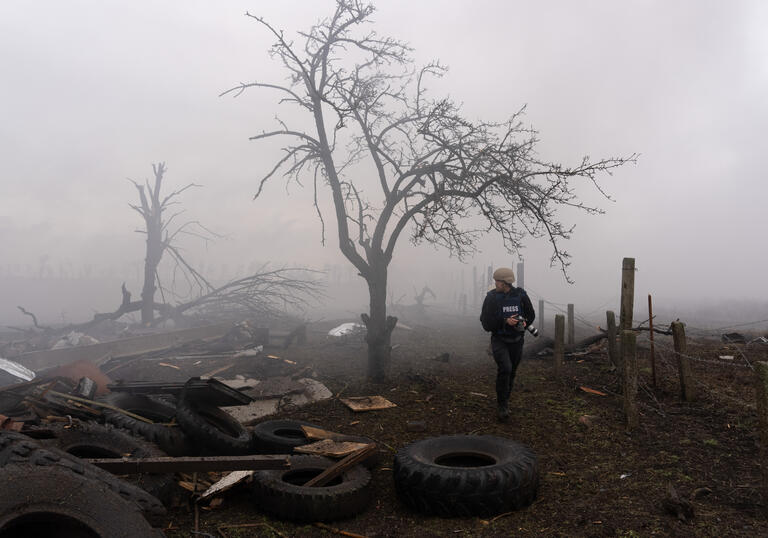 A dark shot of a tree in a war zone. The sky is hazy.
