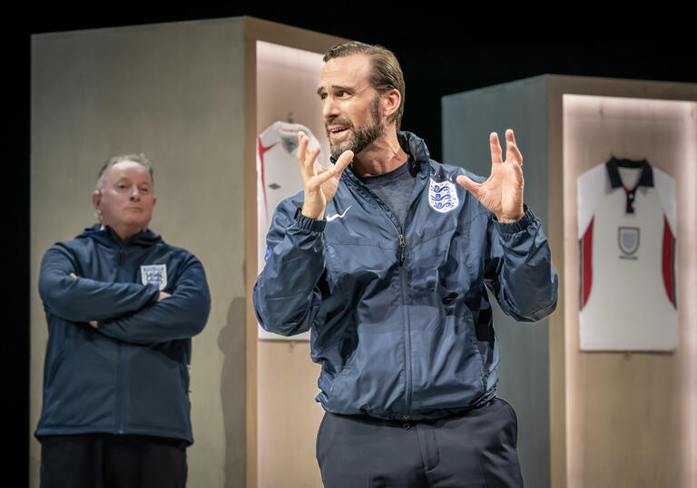 A man in a football tracksuit talks passionately in the locker room. 