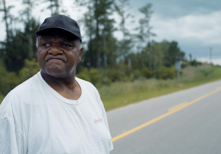 A man wearing a black cap looks down a long road in South Carolina.