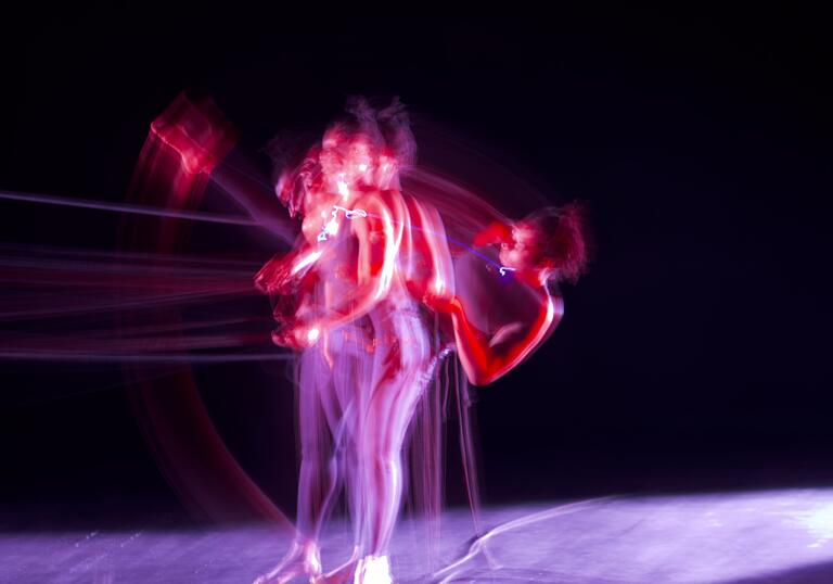 Performer Julene Robinson is photographed on stage doing a high kick, you can see various versions of her in a blur.