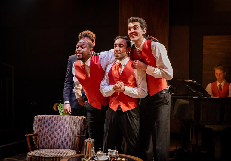 Three singers in red waistcoats, with grand piano in background