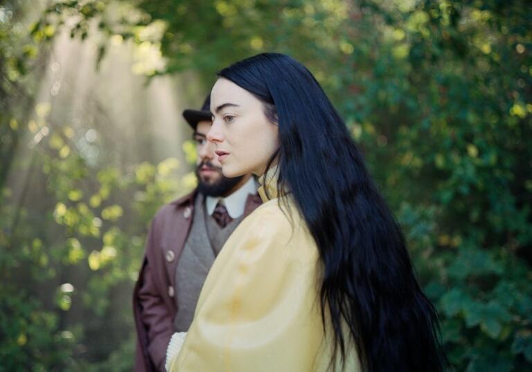 A woman stands in a forest in a yellow dress.