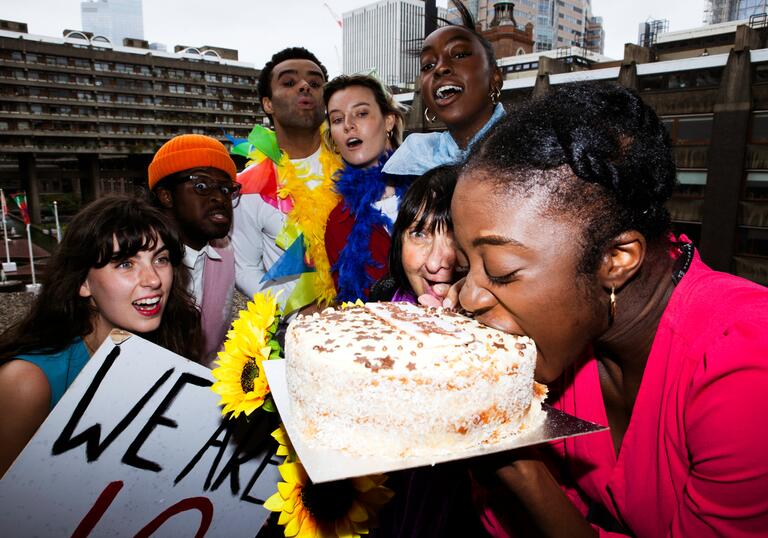 The PappyShow company watch as one member bites into a big birthday cake.