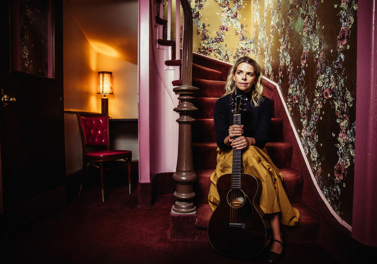 Aoife O'Donovan sits on purple staircase holding guitar