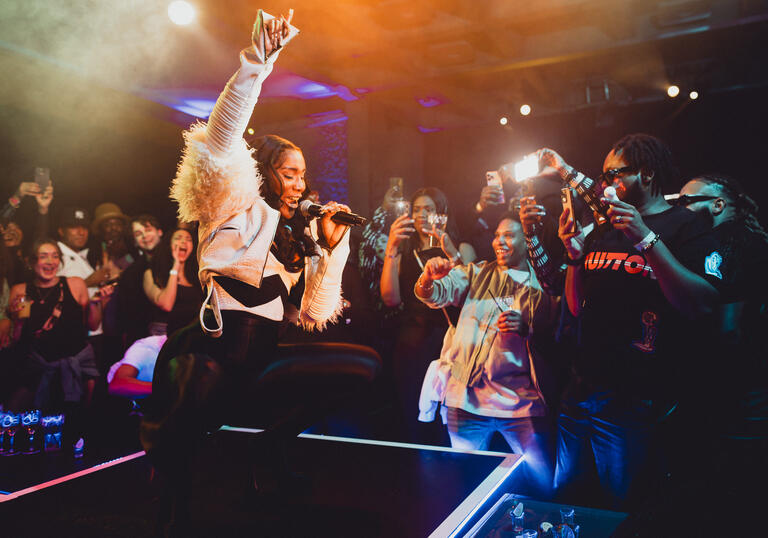 Performer Alicai Harley squatting with arm in the air while singing on stage