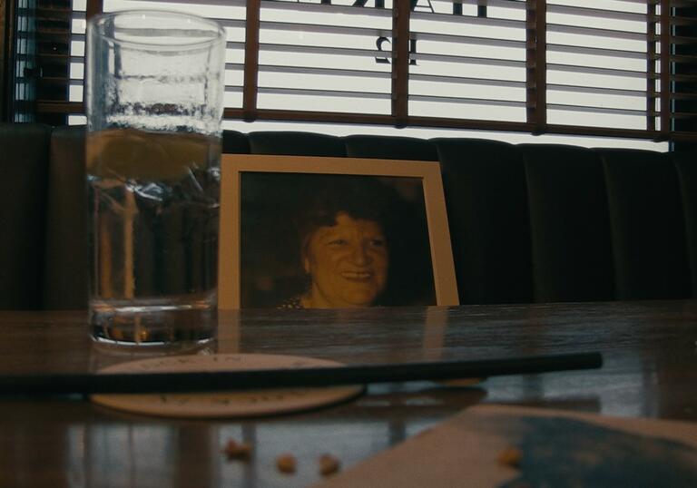 A portrait of a woman sits on a bar seat in a pub. 