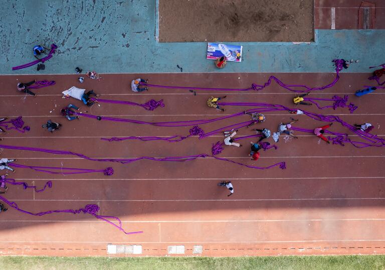 workers in a football stadium assemble a large purple piece of material