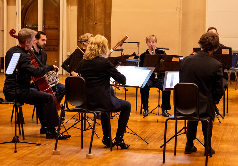 A small selection of musicians from Britten Sinfonia seated in a semi-circle, playing their instruments