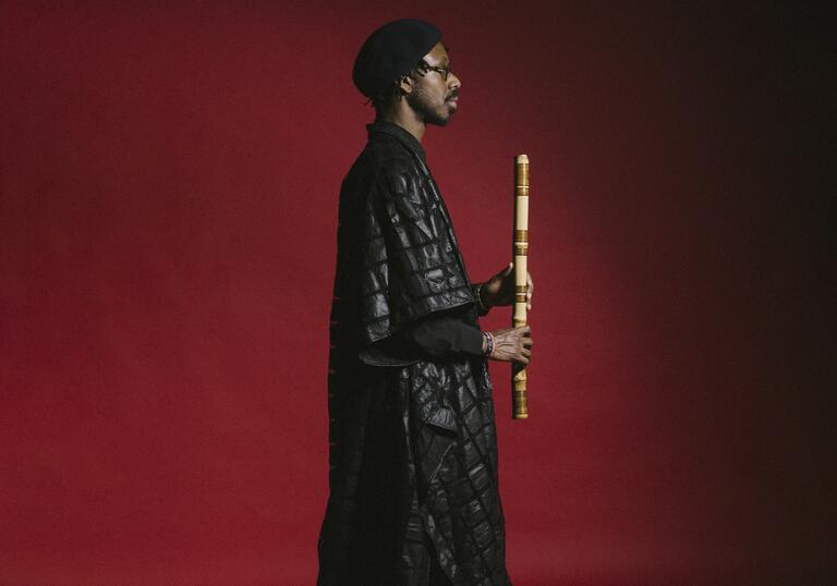 Shabaka Hutchings stands in profile against a red background