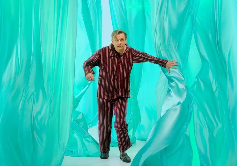 A man in pyjamas bursts through a turquoise dreamscape. 