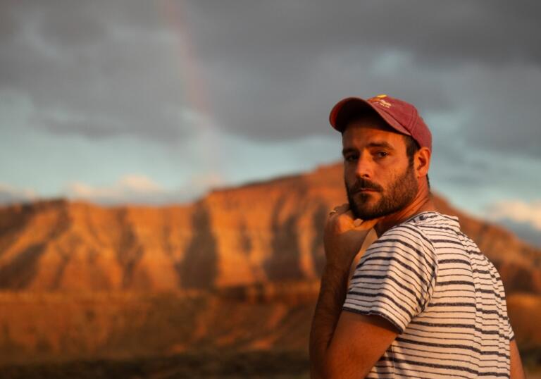 Roo Panes looks over his shoulder at the camera, surrounded by a rugged landscape