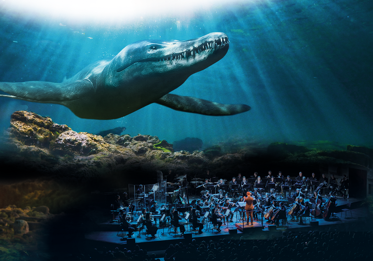 On the bottom right of the image, an orchestra is performing on stage. Behind them is a projection of a still from Life on Our Planet, showing a huge shark appearing to swim towards the audience.