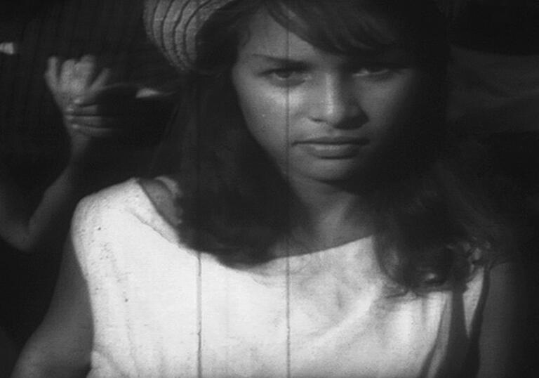 A young woman looks forward towards the camera in an aged, black and white photograph.