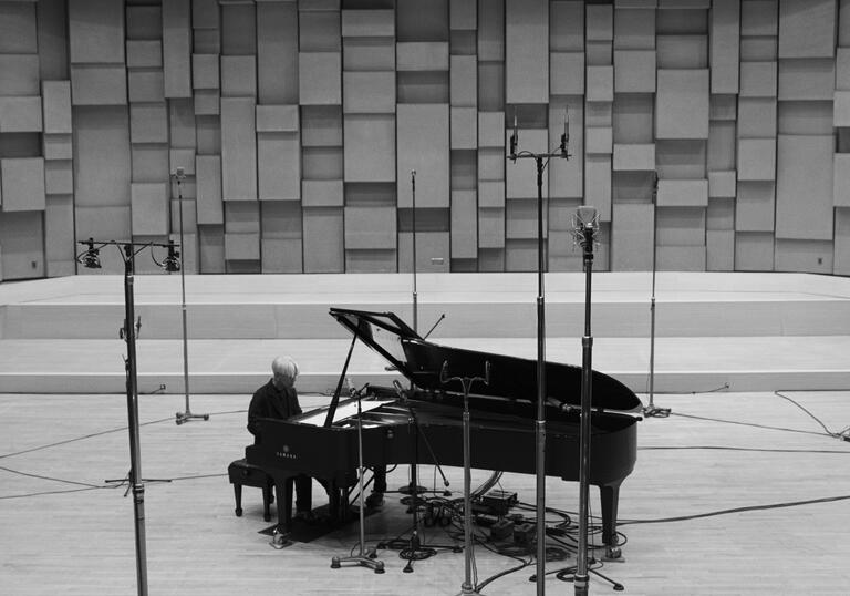 A man sits at a grand piano on a large stage.